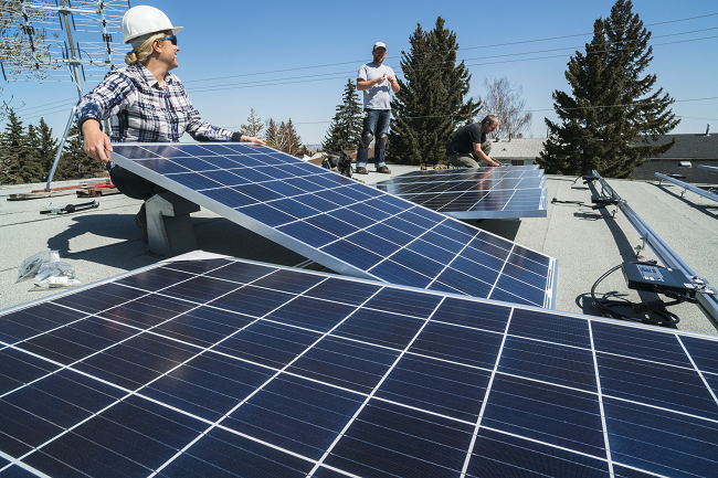 Two workers in hard hats installing solar panels on the roof of a house.